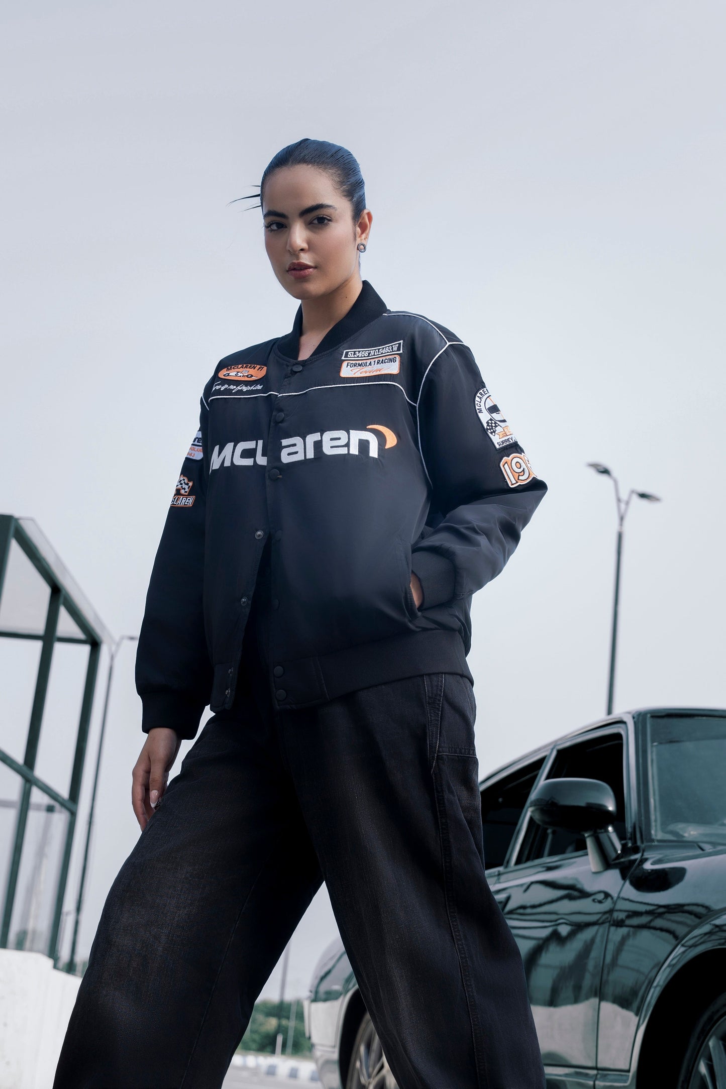 Model wearing a Koti Apparels black McLaren F1 racing jacket with premium embroidery and full-zip front outdoors.