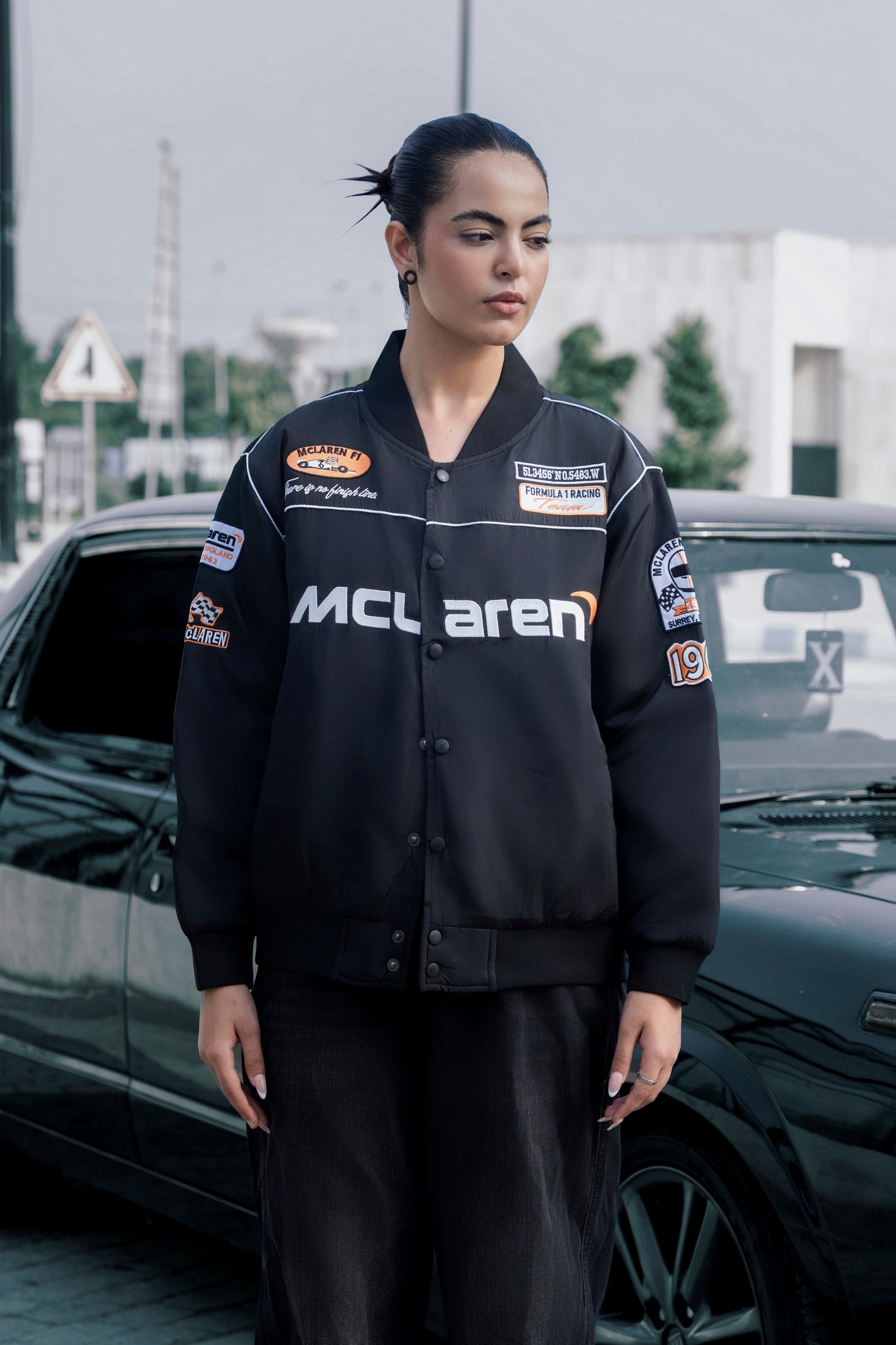 Koti Apparels black McLaren F1 racing jacket with premium needle embroidery, worn by a model outdoors.
