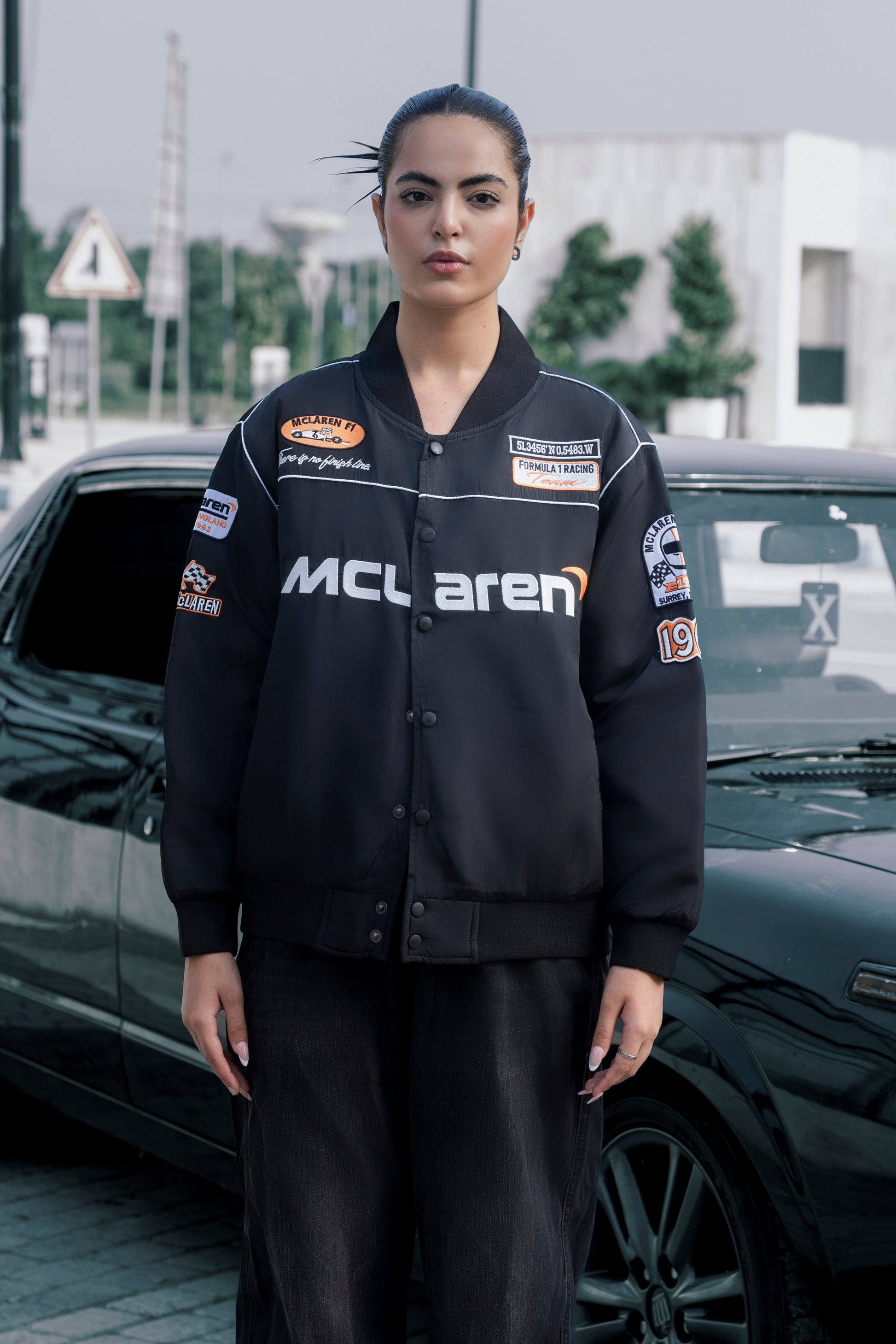 Model wearing a black Koti Apparels McLaren F1 racing jacket with premium needle-embroidered logos and zip front.