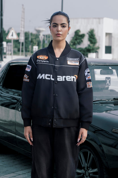 Model wearing a black Koti Apparels McLaren F1 racing jacket with premium needle-embroidered logos and zip front.