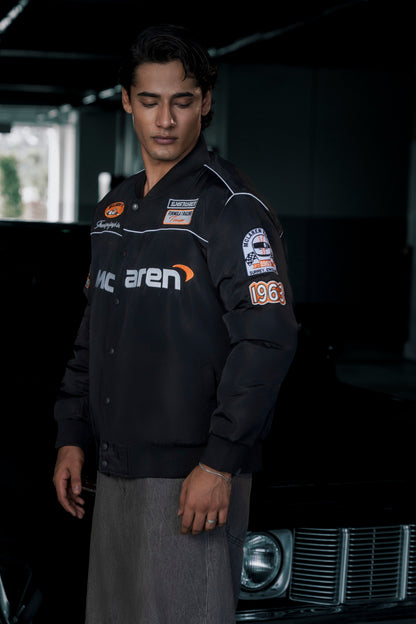 Male model wearing a black Koti Apparels McLaren F1 racing jacket with premium embroidered logos and quilted lining.