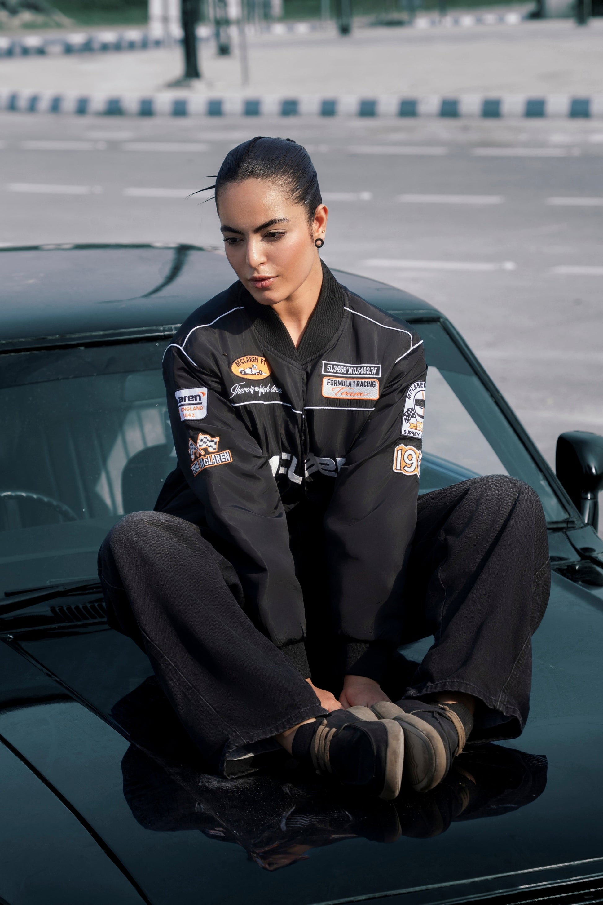 Koti Apparels McLaren F1 racing jacket in black waterproof fabric with detailed embroidery, worn by a model on a car.