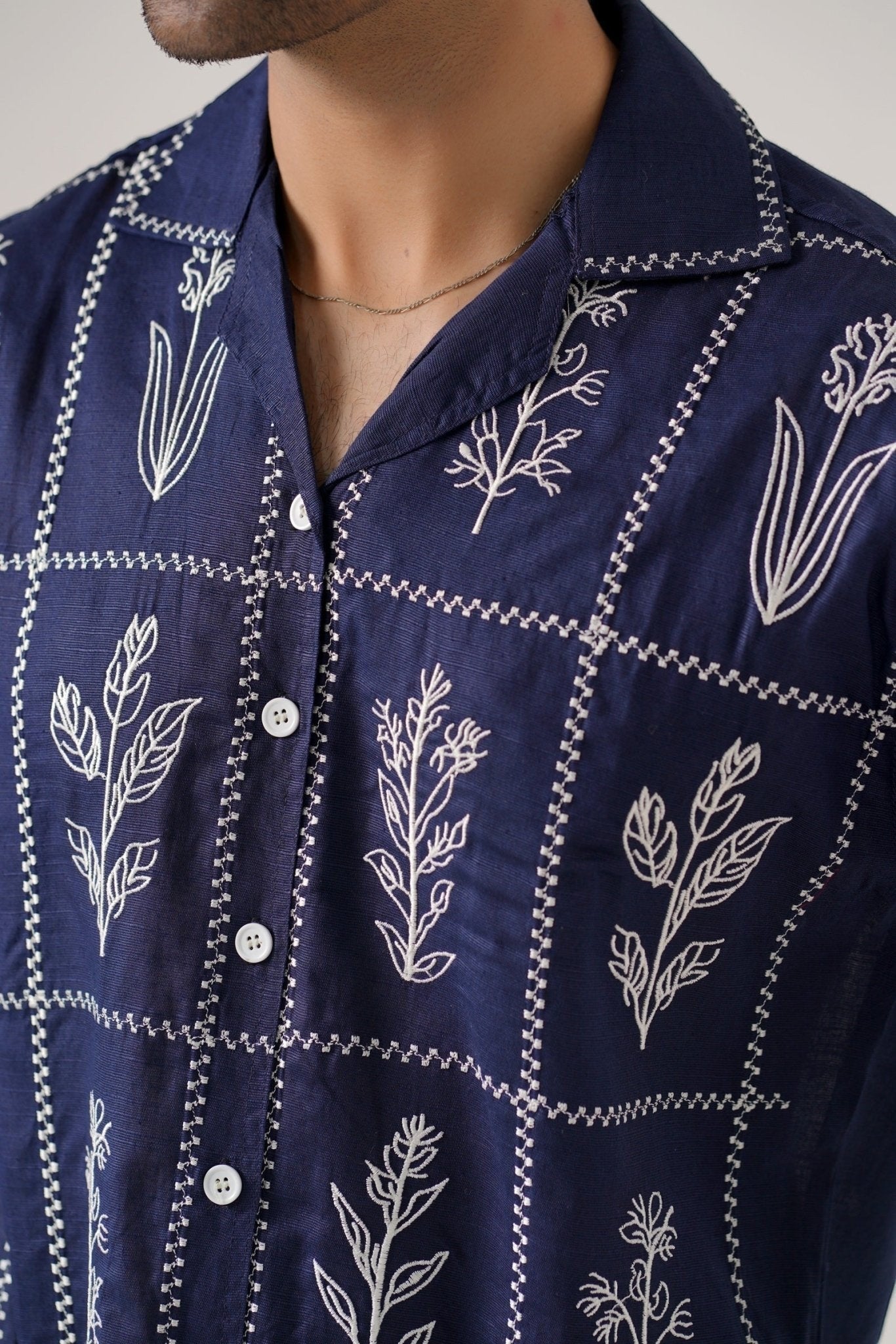 Koti Apparels navy blue cotton khaddar unisex shirt with ivory-white floral embroidery in a grid pattern and open collar.