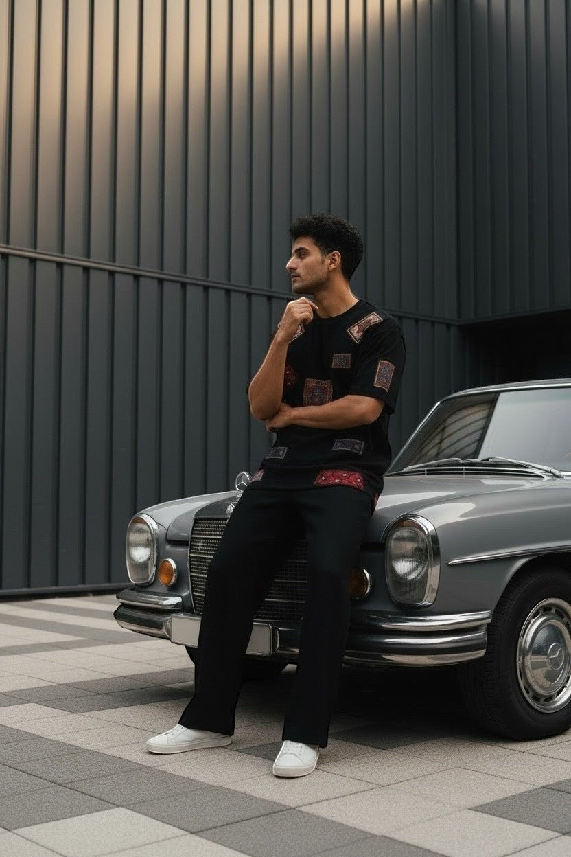 Koti Apparels black cotton t-shirt with patchwork oriental rug graphic details, relaxed fit, worn by a man sitting on a vintage car.