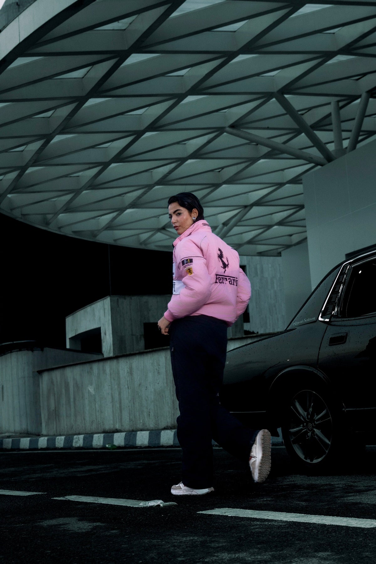 Koti Apparels pink Ferrari puffer jacket with racing embroidery worn by a model standing near a black car