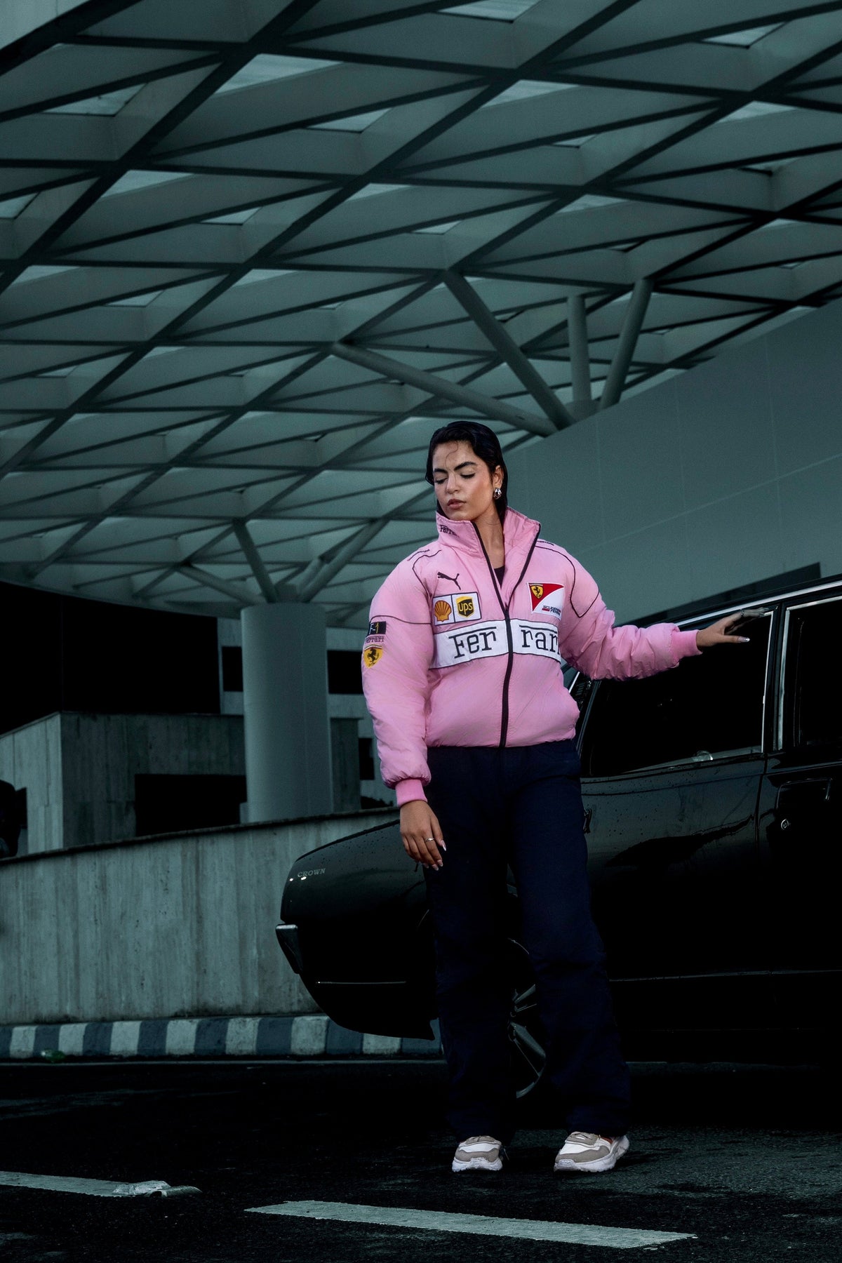 Koti Apparels pink Ferrari racing jacket with embroidered logos worn by a woman standing next to a black car