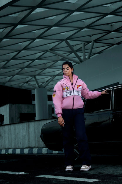 Koti Apparels pink Ferrari racing jacket with embroidered logos worn by a woman standing next to a black car