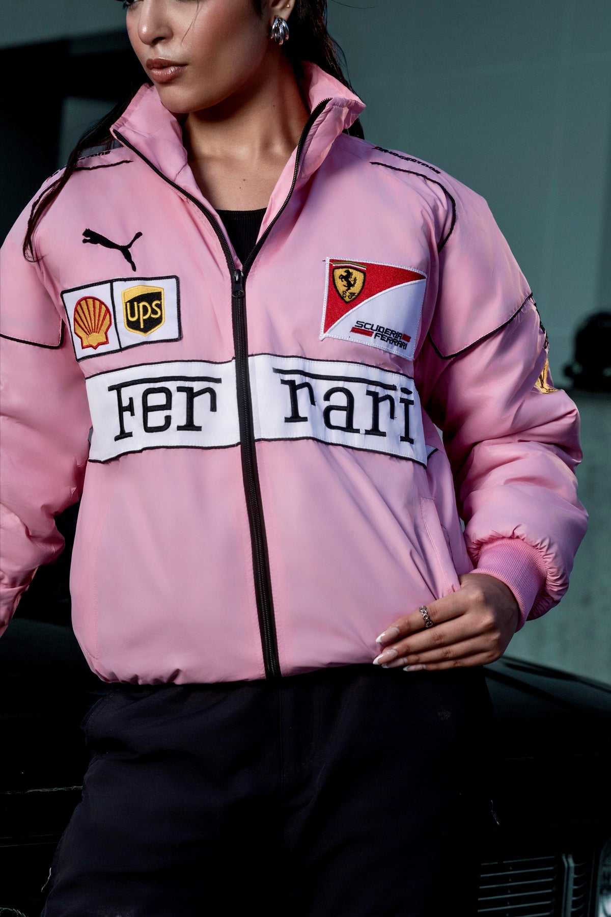 Model wearing a vibrant pink Koti Apparels Ferrari racing jacket with embroidered F1 sponsor logos and a zip front.