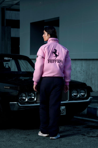 Model wearing a pink Koti Apparels Ferrari racing jacket with black embroidered logos, standing by a vintage car.