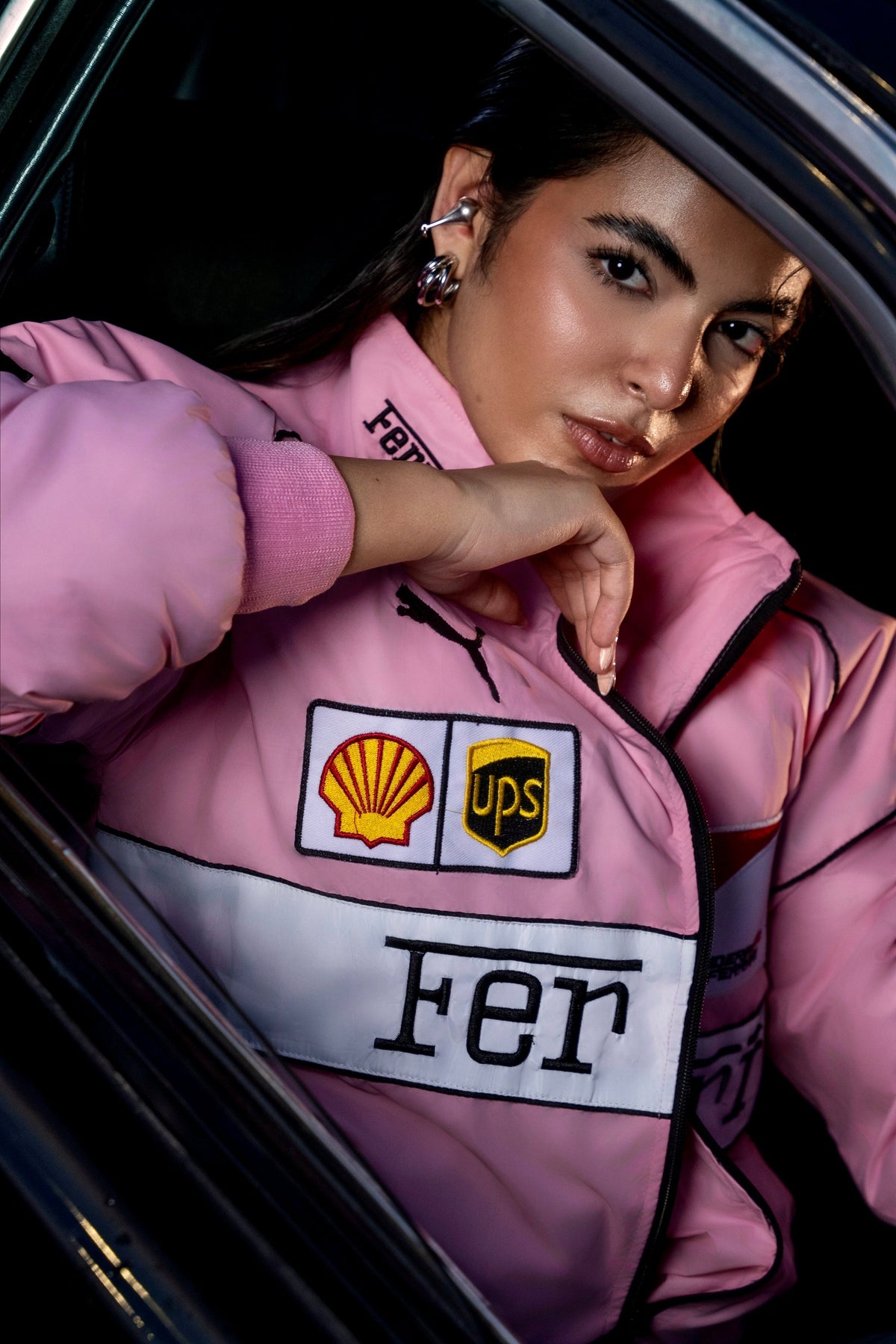 Koti Apparels pink Ferrari racing jacket with embroidered sponsor logos worn by a woman inside a car