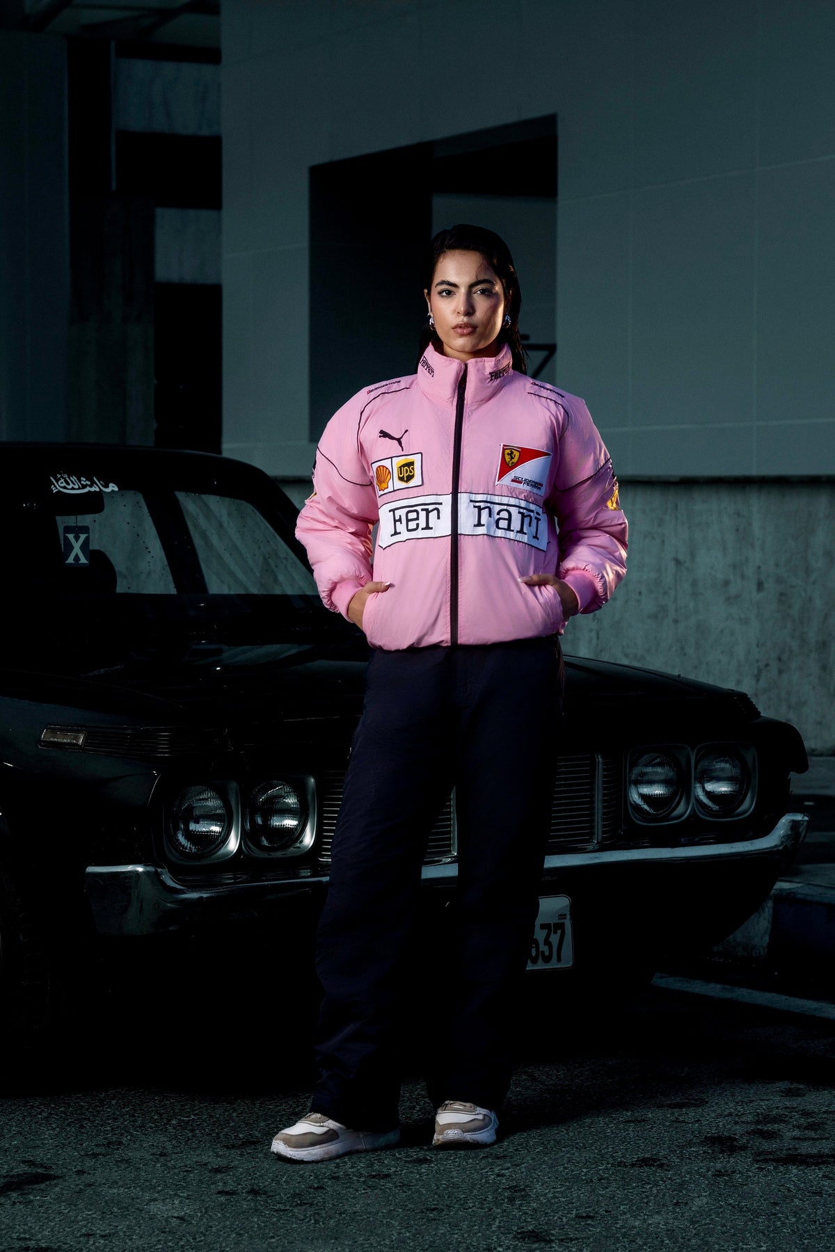 Koti Apparels pink Ferrari racing jacket with embroidered logos worn by a woman standing in front of a black car