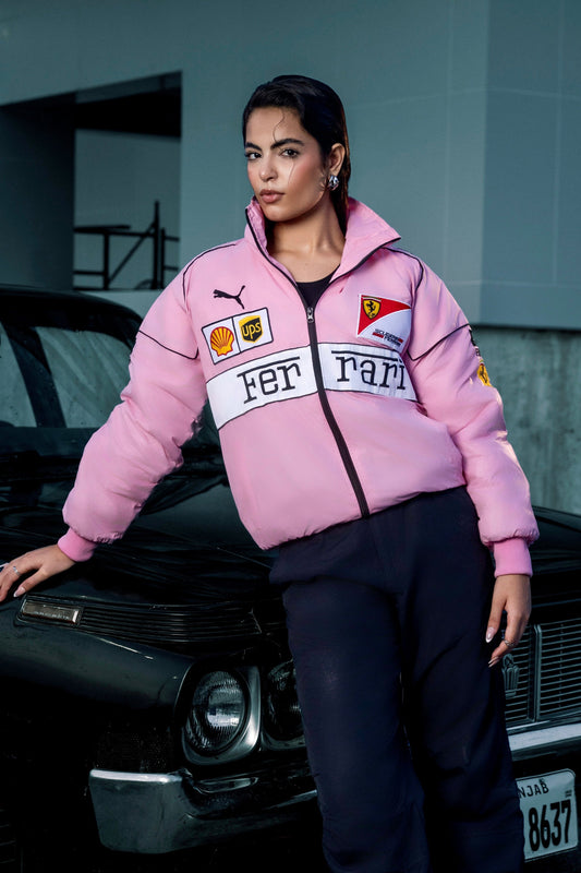 Koti Apparels pink Ferrari racing jacket with embroidered logos worn by a woman leaning against a black car