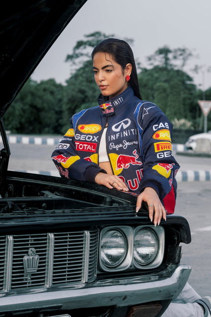 Koti Apparels Red Bull racing jacket with embroidered sponsor logos worn by a woman leaning on a vintage car hood