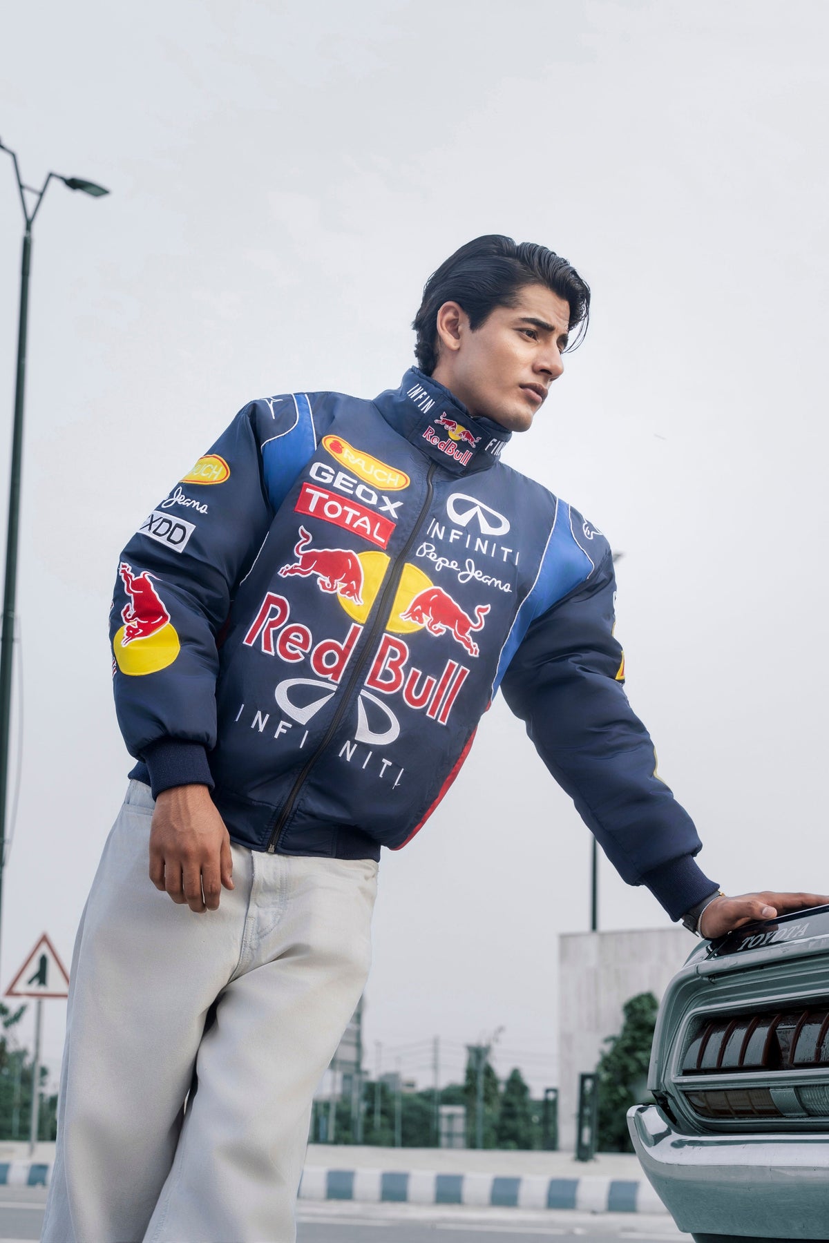 Koti Apparels navy blue Red Bull racing jacket with embroidered team logos worn by a man leaning against a car
