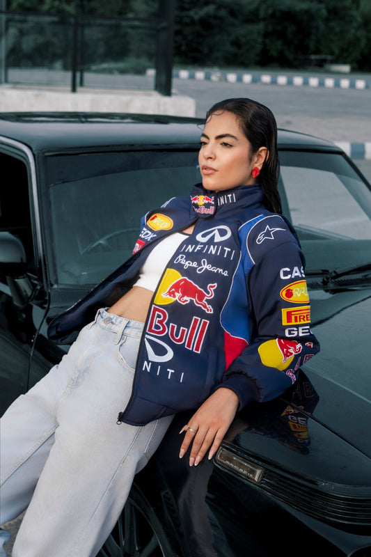 Model wearing a Koti Apparels Red Bull racing jacket with embroidered team logos, styled with light wash jeans.