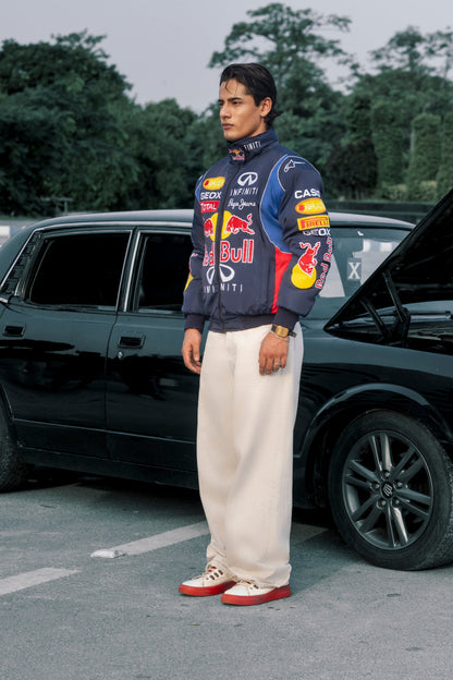 Koti Apparels Red Bull racing jacket with embroidered logos worn by a man standing next to a black car.