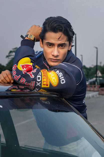 Koti Apparels navy blue Red Bull racing jacket with authentic embroidered sponsor logos worn by a man leaning on a car
