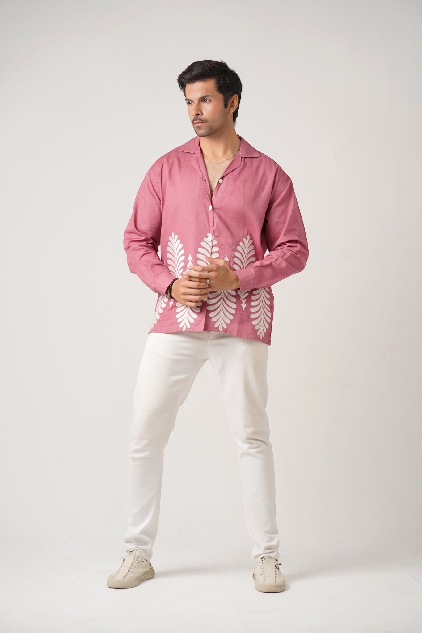 Koti Apparels rose pink unisex shirt with full sleeves, spread collar, and white leaf embroidery on the hem. Model wears white pants.