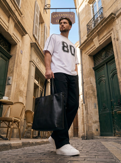 Koti Apparels white cotton down shoulder t-shirt with black 80 graphic and piping, worn by a man in a city street.