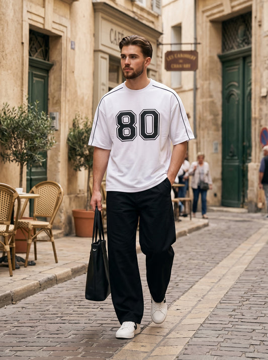 Koti Apparels white cotton down shoulder t-shirt with black 80 graphic and piping worn by a man on a city street