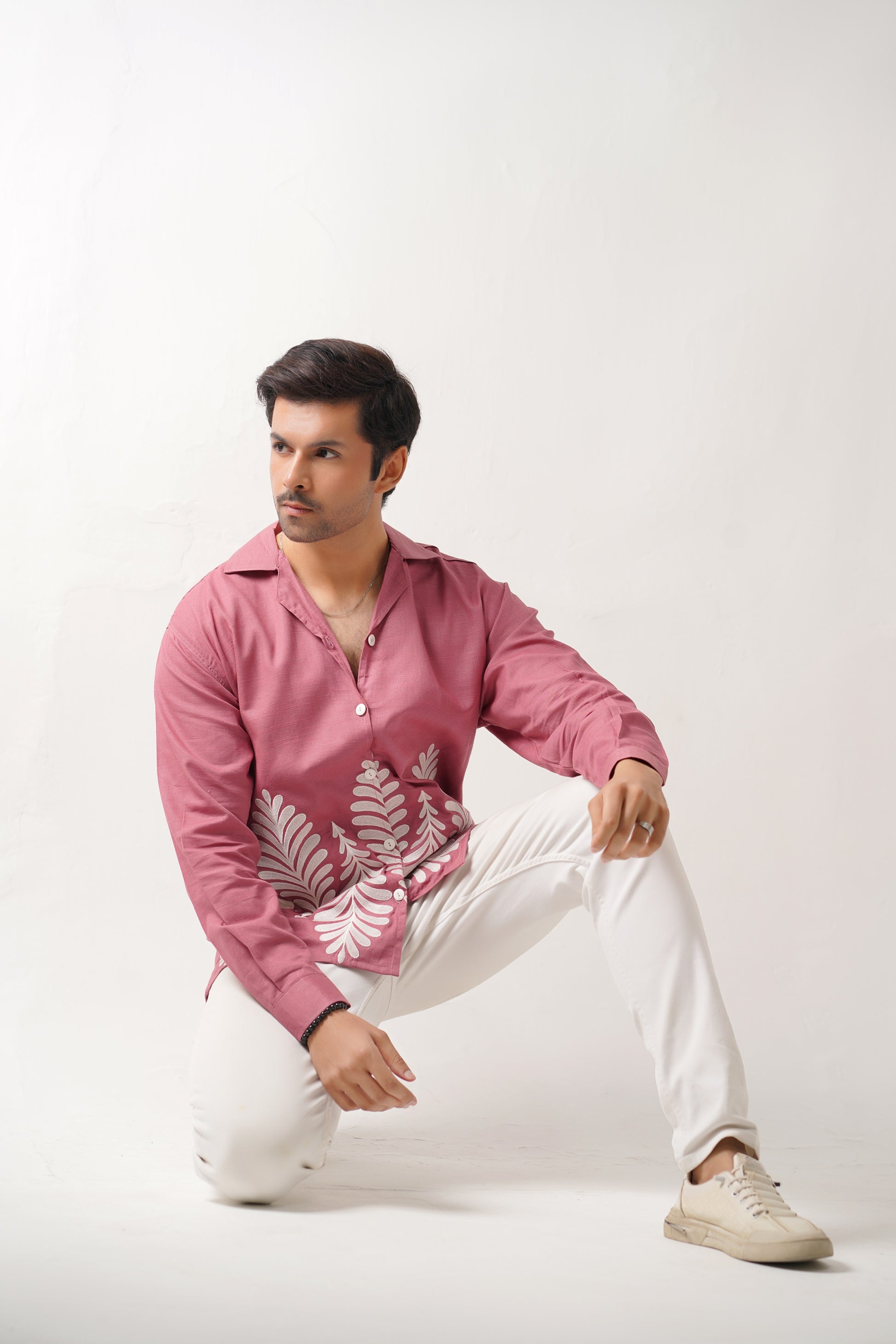 Man wearing a pink embroidered shirt and white pants on a white background