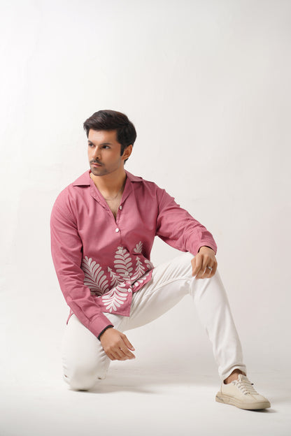 Man wearing a pink embroidered shirt and white pants on a white background