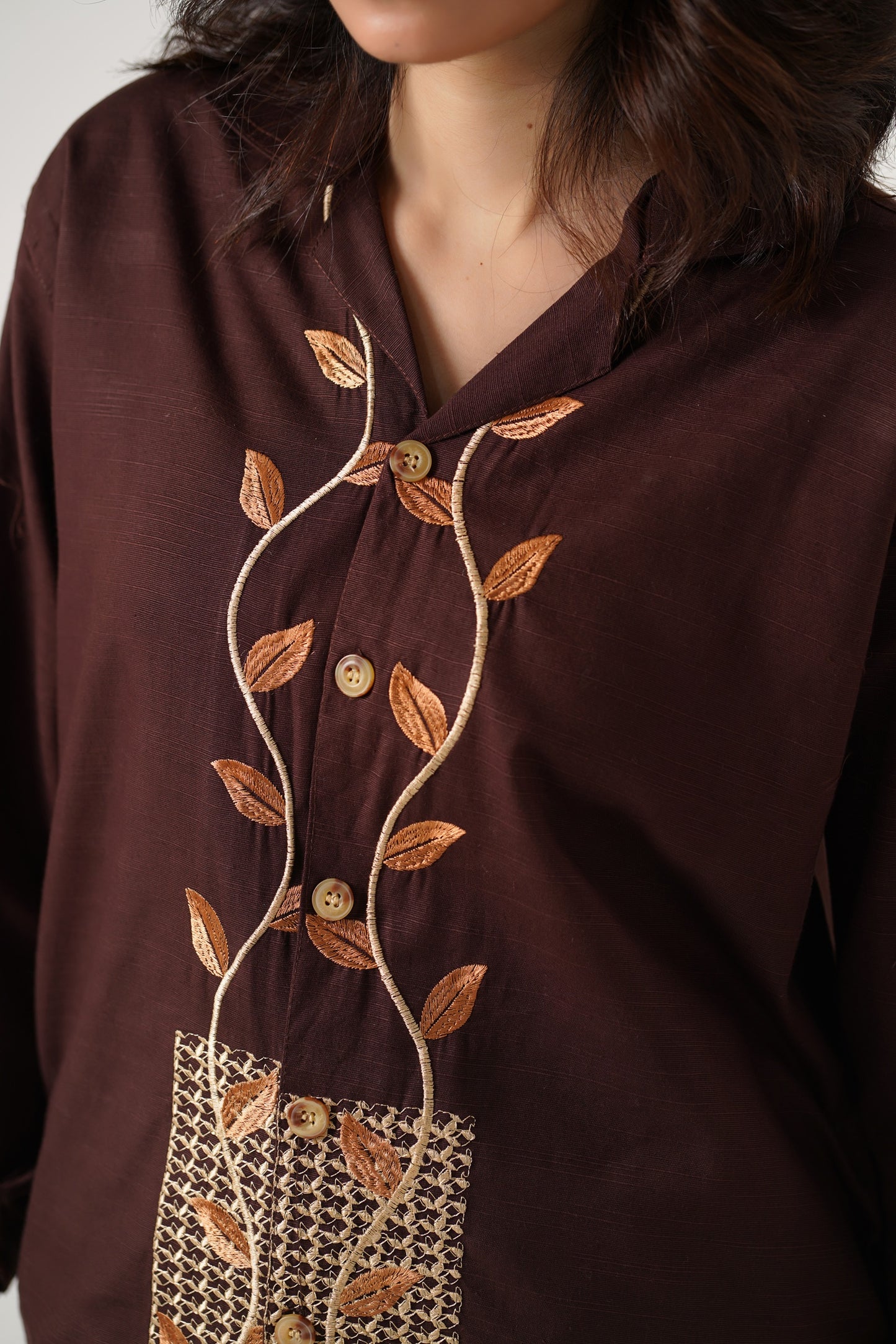 Brown blouse with leaf embroidery and buttons on a plain background