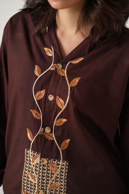 Brown blouse with leaf embroidery and buttons on a plain background