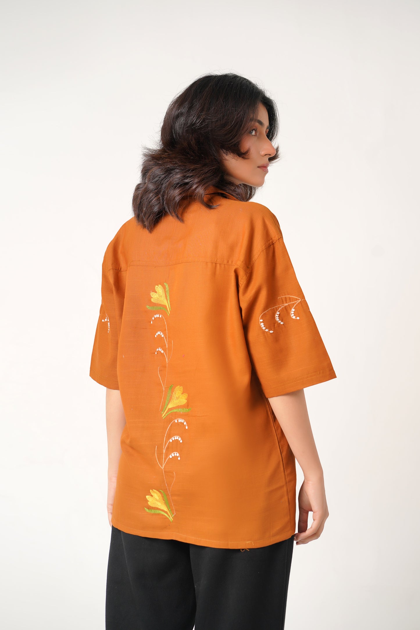 Woman wearing an orange shirt with floral designs on a white background