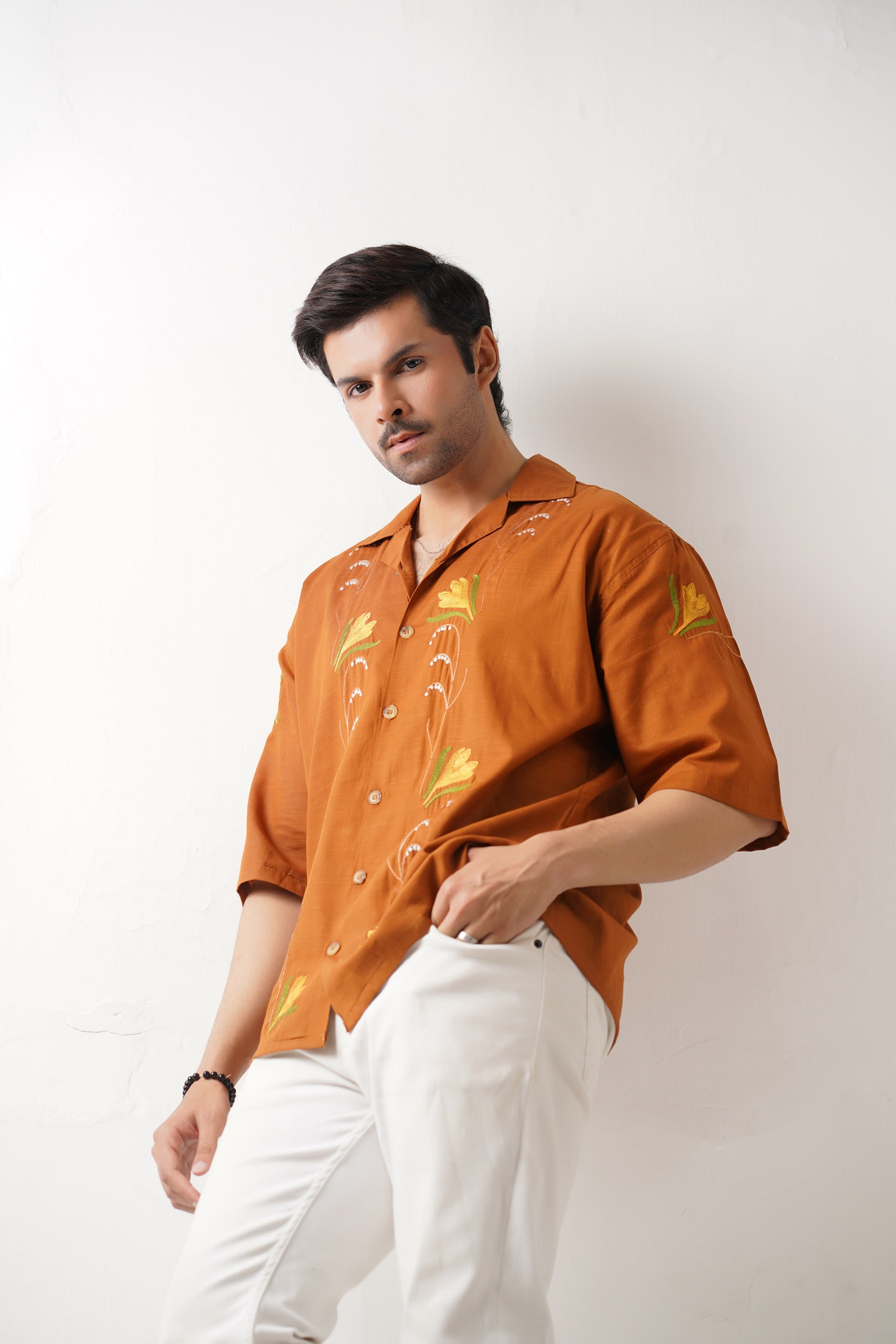 Man wearing an orange shirt with floral patterns and white pants on a white background