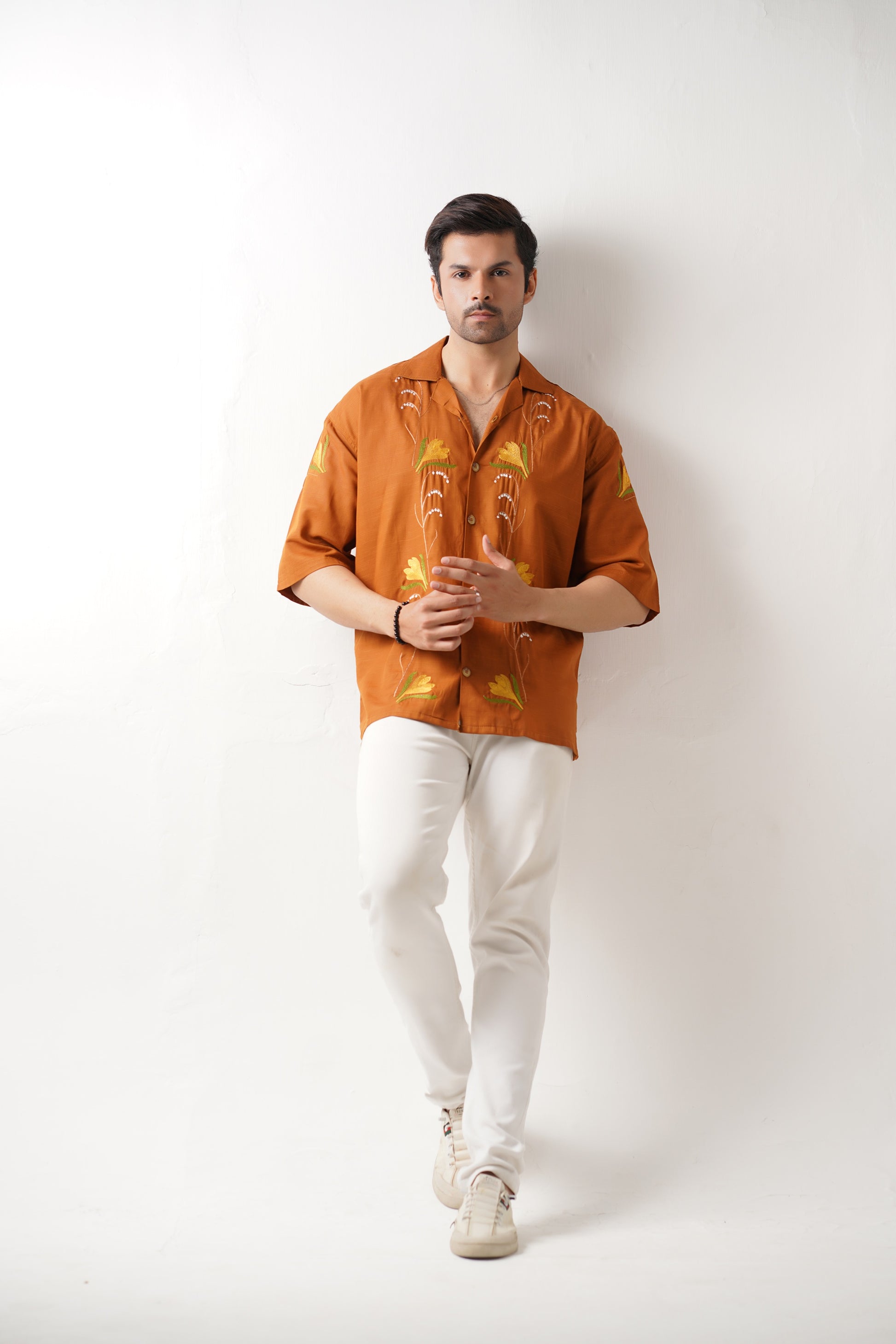 Man wearing an orange patterned shirt and white pants against a white background