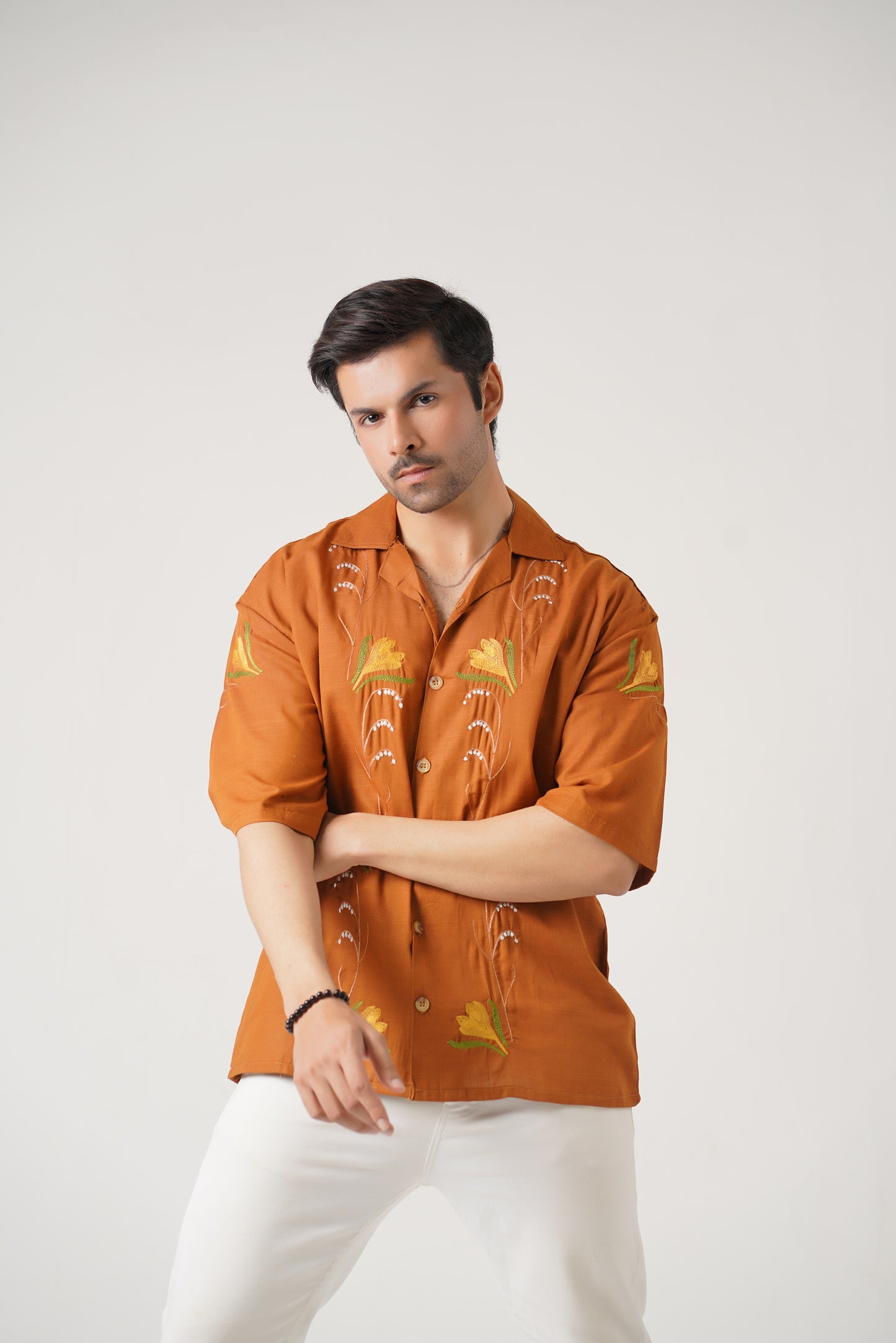 Man wearing an orange embroidered shirt with white pants on a light gray background