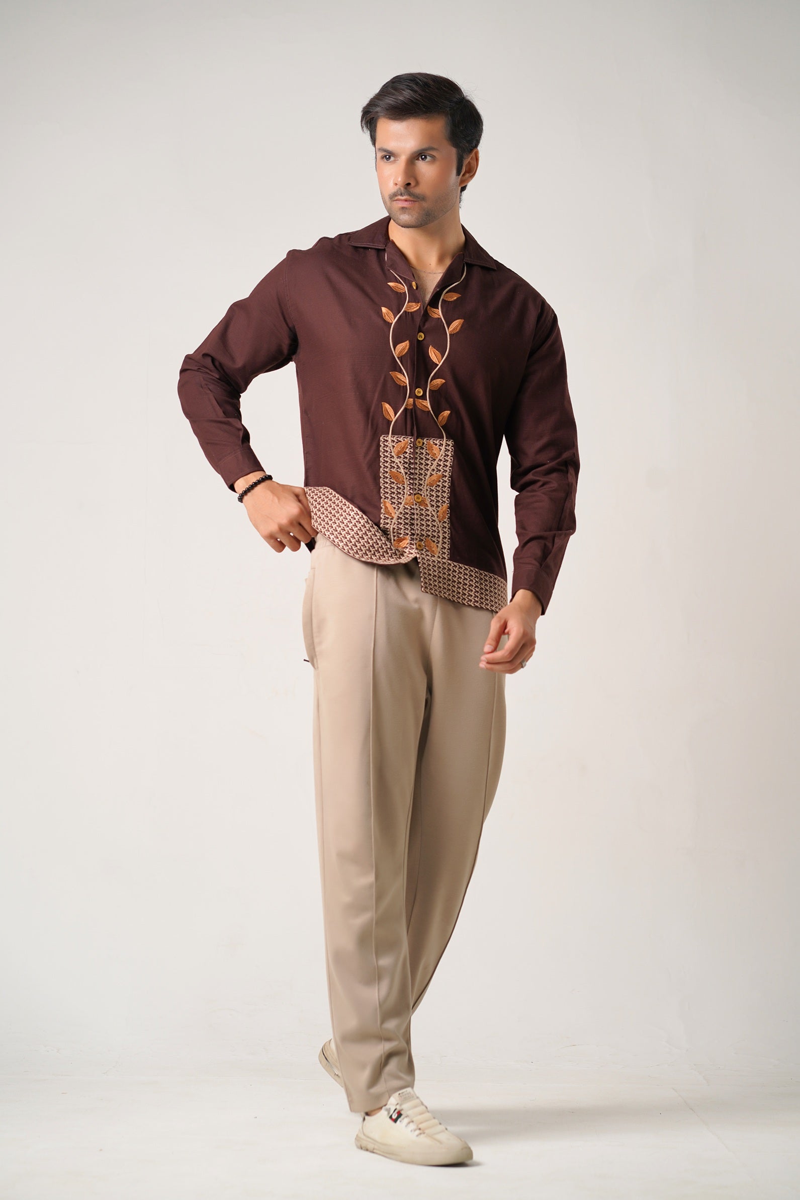 Man wearing a brown patterned shirt and beige pants on a white background