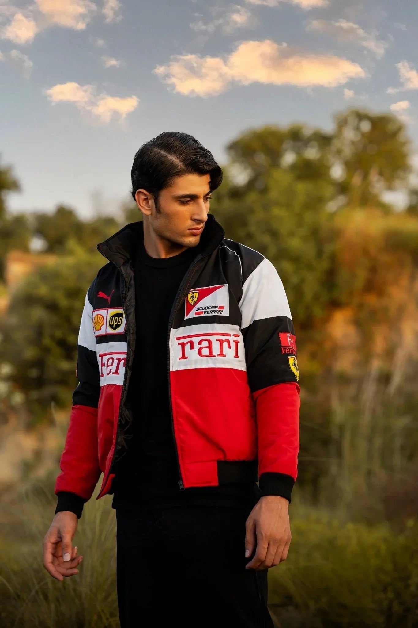 A man wearing a Formula 1 Ferrari jacket with a red and black color scheme, featuring embroidered Ferrari and F1 logos.
