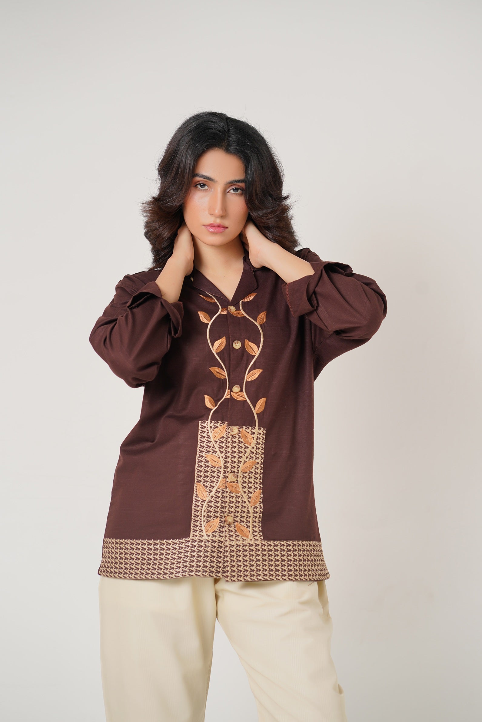 Woman wearing a brown blouse with intricate patterns on a plain background