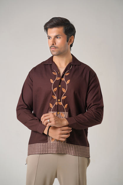 Man wearing a brown embroidered shirt with beige pants on a plain background
